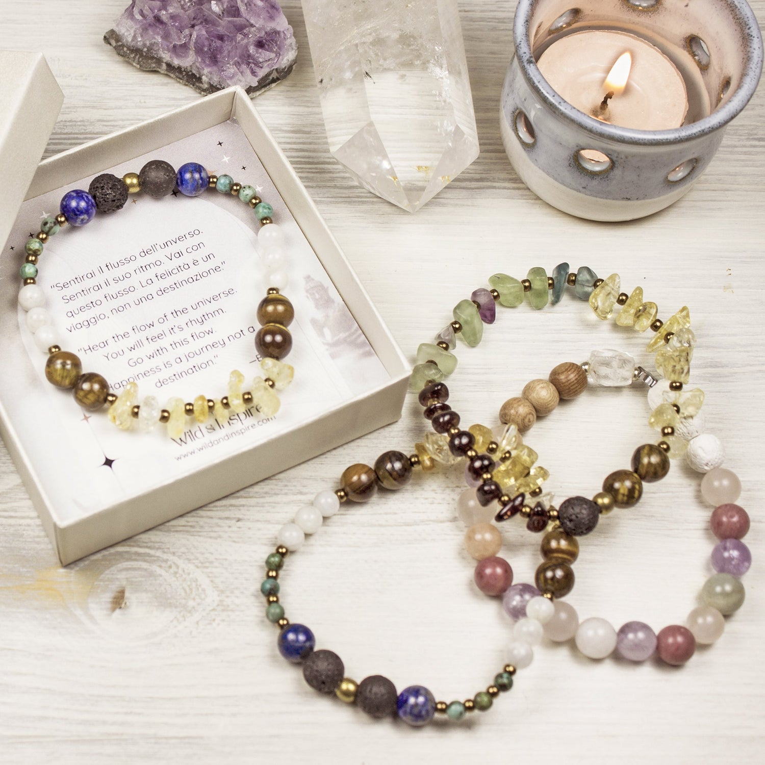 Beaded gemstone bracelets, one in a gift box, on a white wooden background and with a candle and crystals