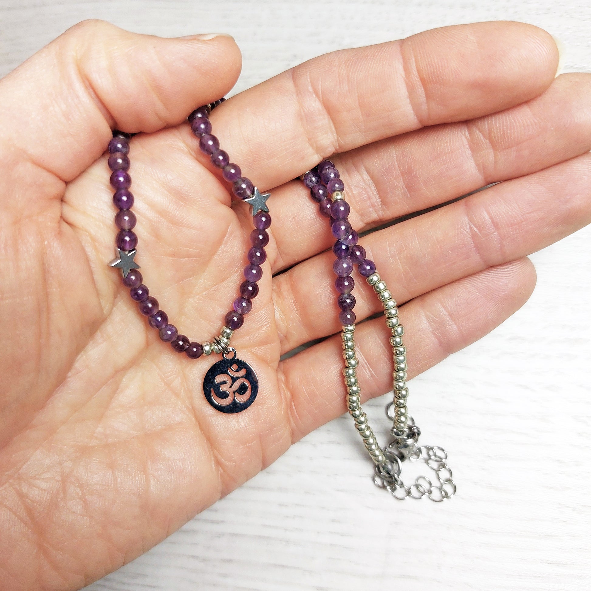 hand holding and amethyst necklace with an om pendant 