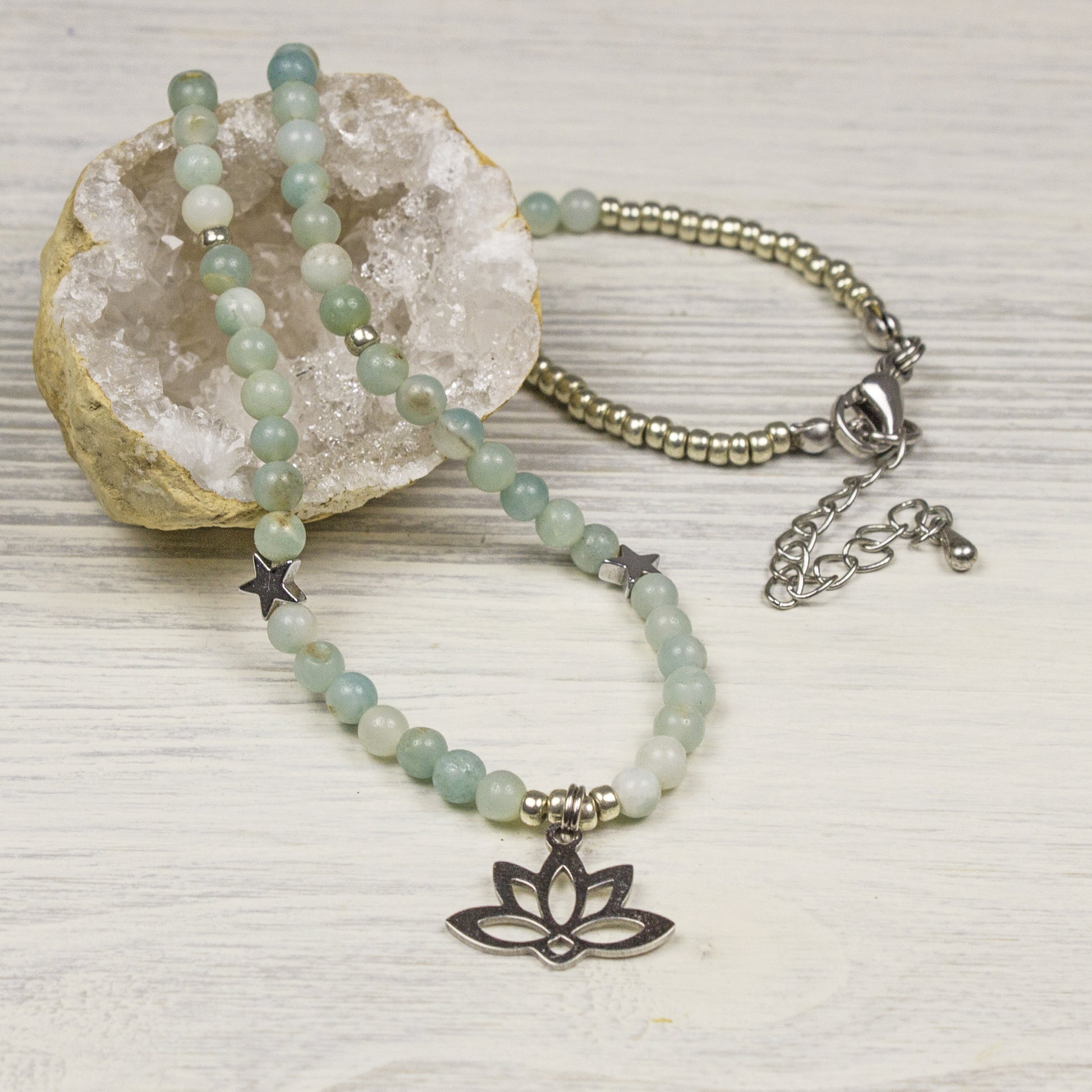 Beaded ammazonite necklace with a silver lotus charm on a white wood backrìground with crystal geode