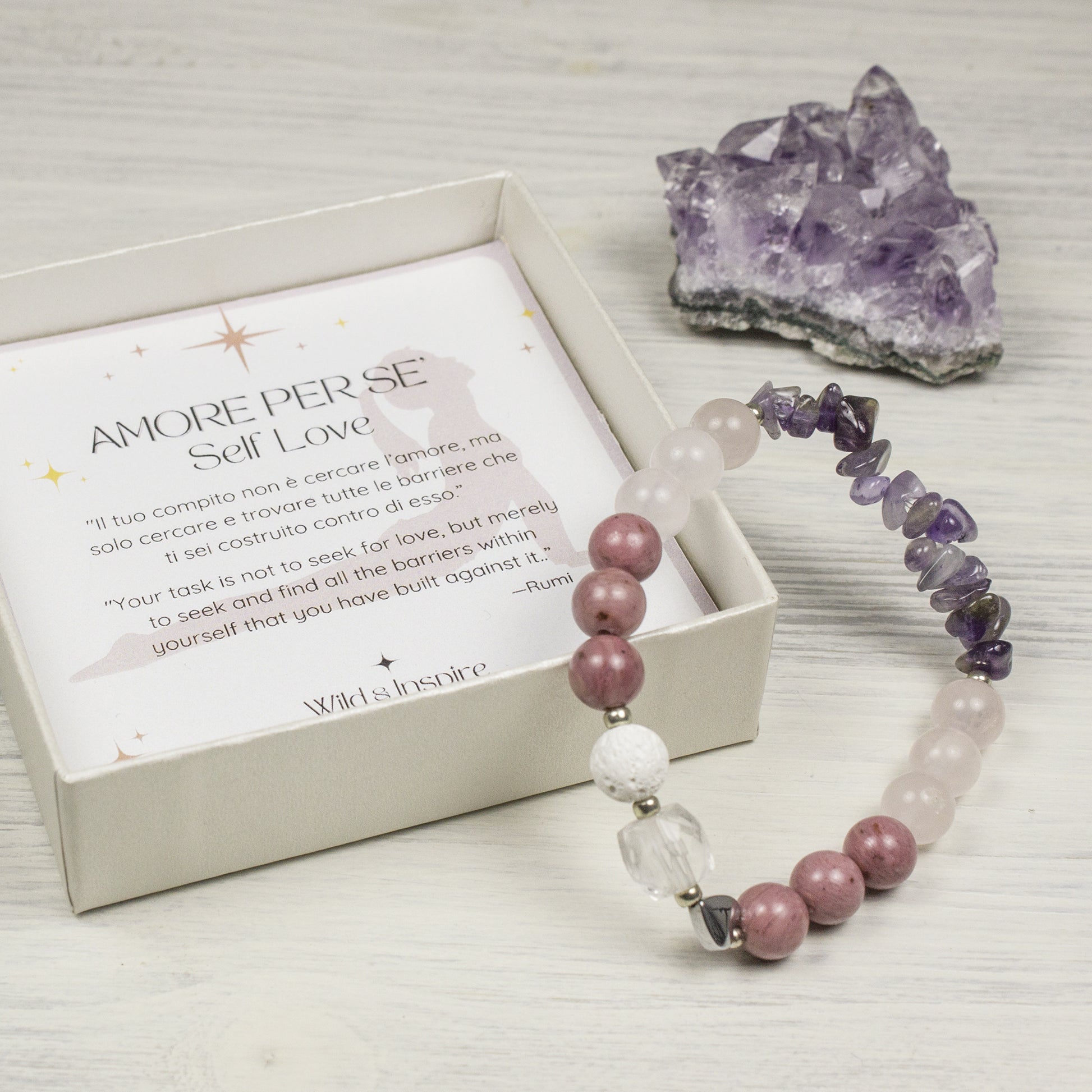Natural stone bracelet with cystals for self love next to a gift box with an affermation card and a n amethyst cluster in the background.