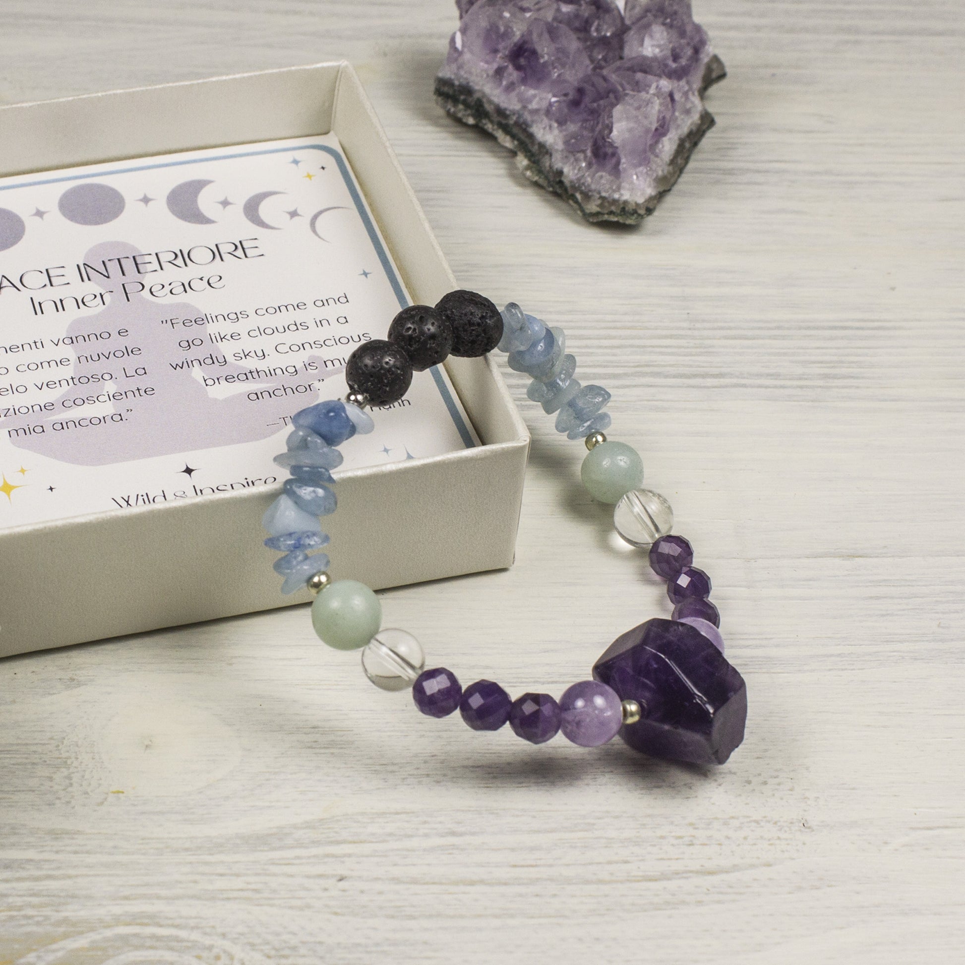 Beaded bracelet with purple and blue stones on a white surface with an affermation card and crystal in the background.