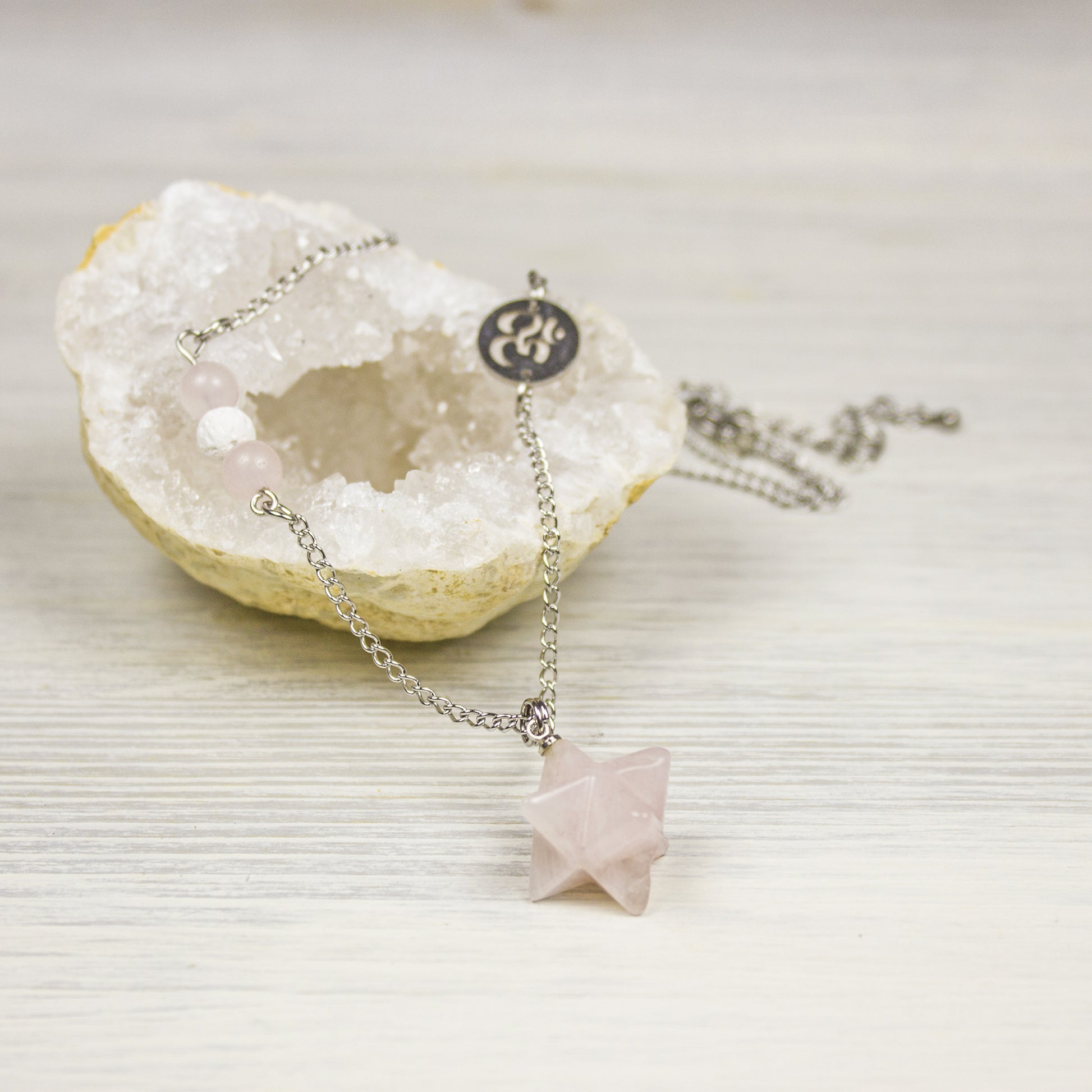 Necklace with a pink crystal pendant and om charm on a white background